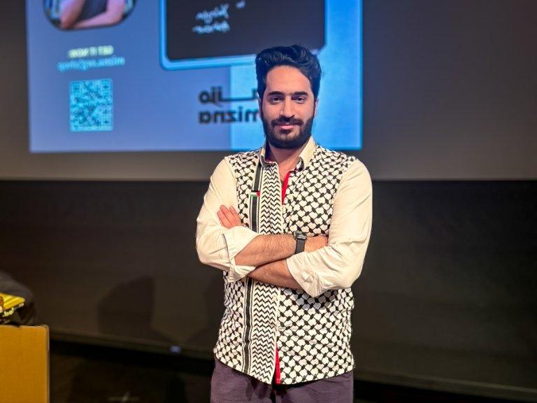 Yahya Ashour stands on the Benson Auditorium stage while wearing a shirt with a black and white keffiyeh pattern.